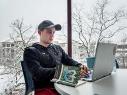 Nursing student sitting in front of a laptop with a book.